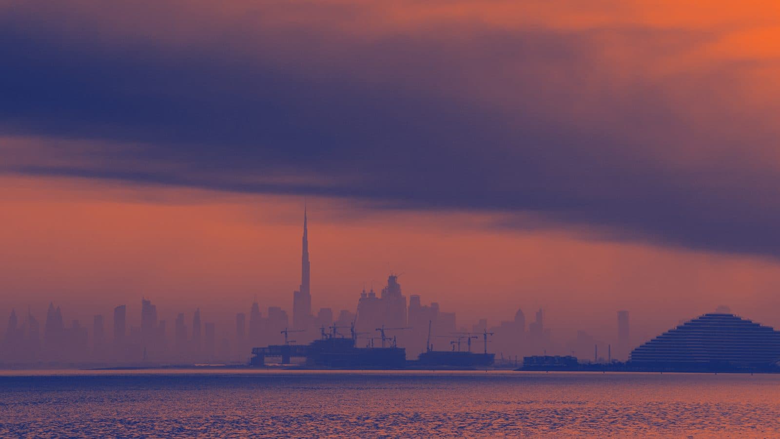 Silhouette of UAE skyline with a prominent tower, silhouetted buildings, and a triangular structure in the foreground. The image has a tone of orange and dark blue.