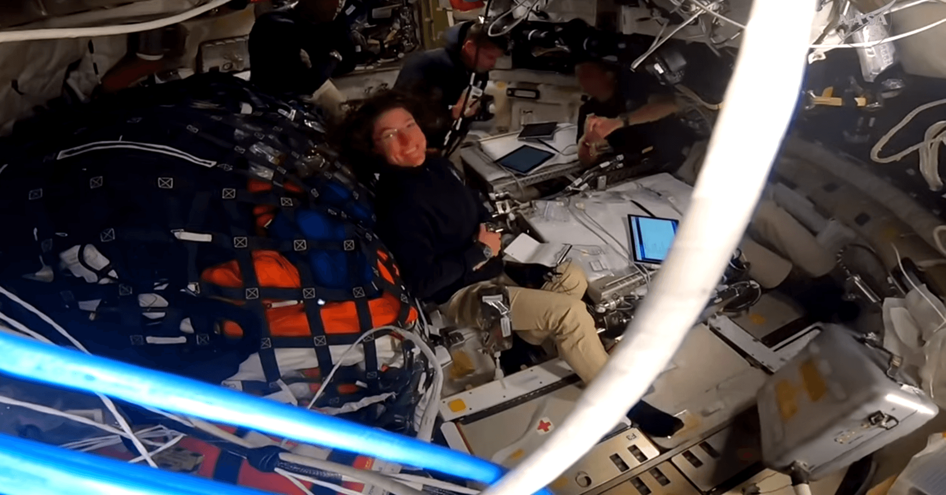 The Artemis II crew floats in Orion; NASA astronaut Christina Koch smiles at the camera as NASA astronaut Reid Wiseman comments on the crew's human spaceflight record. Image is a screenshot from a NASA live broadcast.
